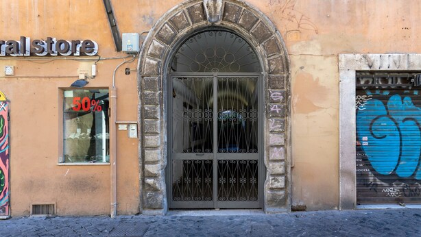 A storefront with a metal gate and a sign indicating a 50% discount. - Designer two-level apartment in the heart of Trastevere (Roma)