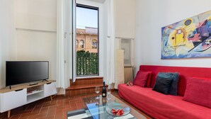 A modern living room with a red sofa, a glass coffee table, a flat-screen TV, and a painting on the wall. - Designer two-level apartment in the heart of Trastevere (Roma)