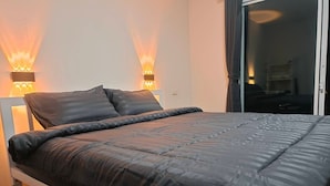 Une chambre moderne avec un grand lit, deux lampes fixées au mur et une porte-fenêtre coulissante donnant sur un balcon.