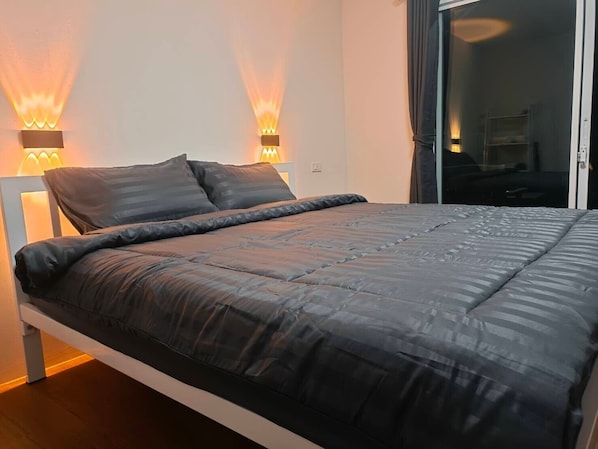 A modern bedroom with a large bed, two wall-mounted lamps, and a sliding glass door leading to a balcony. - The Bay Koh Mook (Ko Mook)