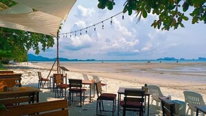 Un restaurant situé en bord de mer, avec une terrasse comprenant des tables et des chaises en bois, le tout abrité par un auvent.
