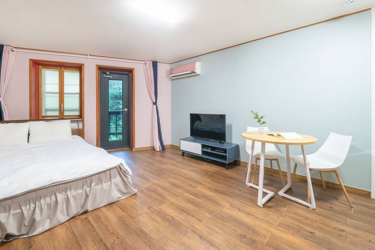 Une chambre à coucher comprenant un lit, une télévision, une petite table avec des chaises et une porte donnant sur un balcon.