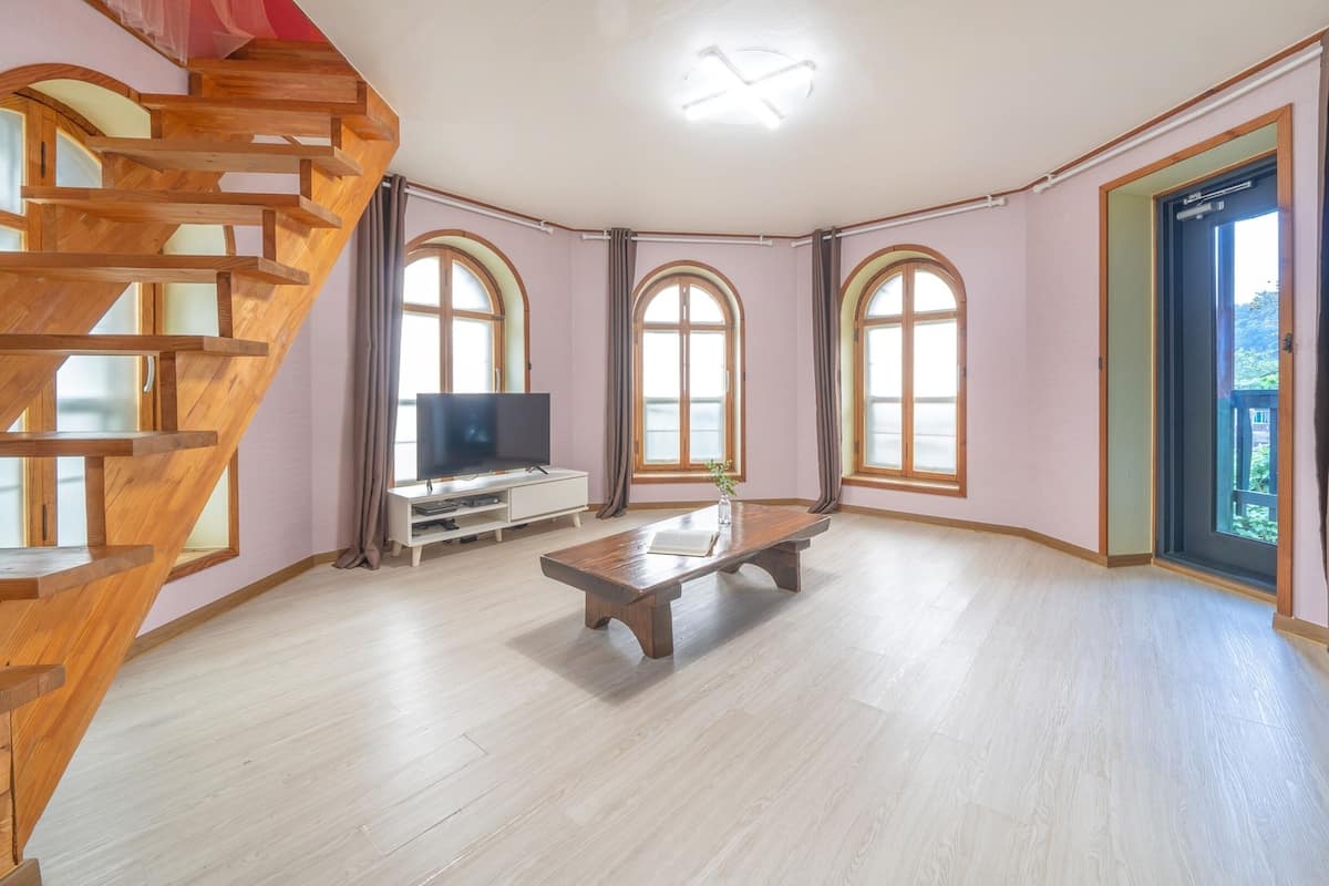 Un salon spacieux avec un escalier en bois, un téléviseur à écran plat, une table basse et de grandes fenêtres en arc de cercle.