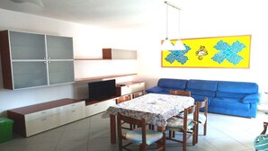 Un salon avec un canapé bleu, une table à manger avec des chaises, un téléviseur et un meuble fixé au mur.