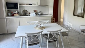 A modern kitchen with white cabinetry, a microwave, and a dining area with a white table and chairs. - Casa Luisa  1 - Casa Luisa 1 (Marciana)