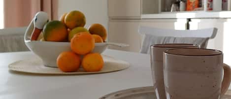 A dining table with a bowl of oranges and lemons, two ceramic mugs, and a tray.
