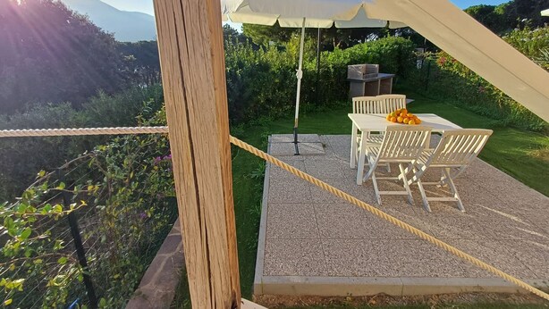 An outdoor patio with a table and chairs, a white umbrella, and a grill.