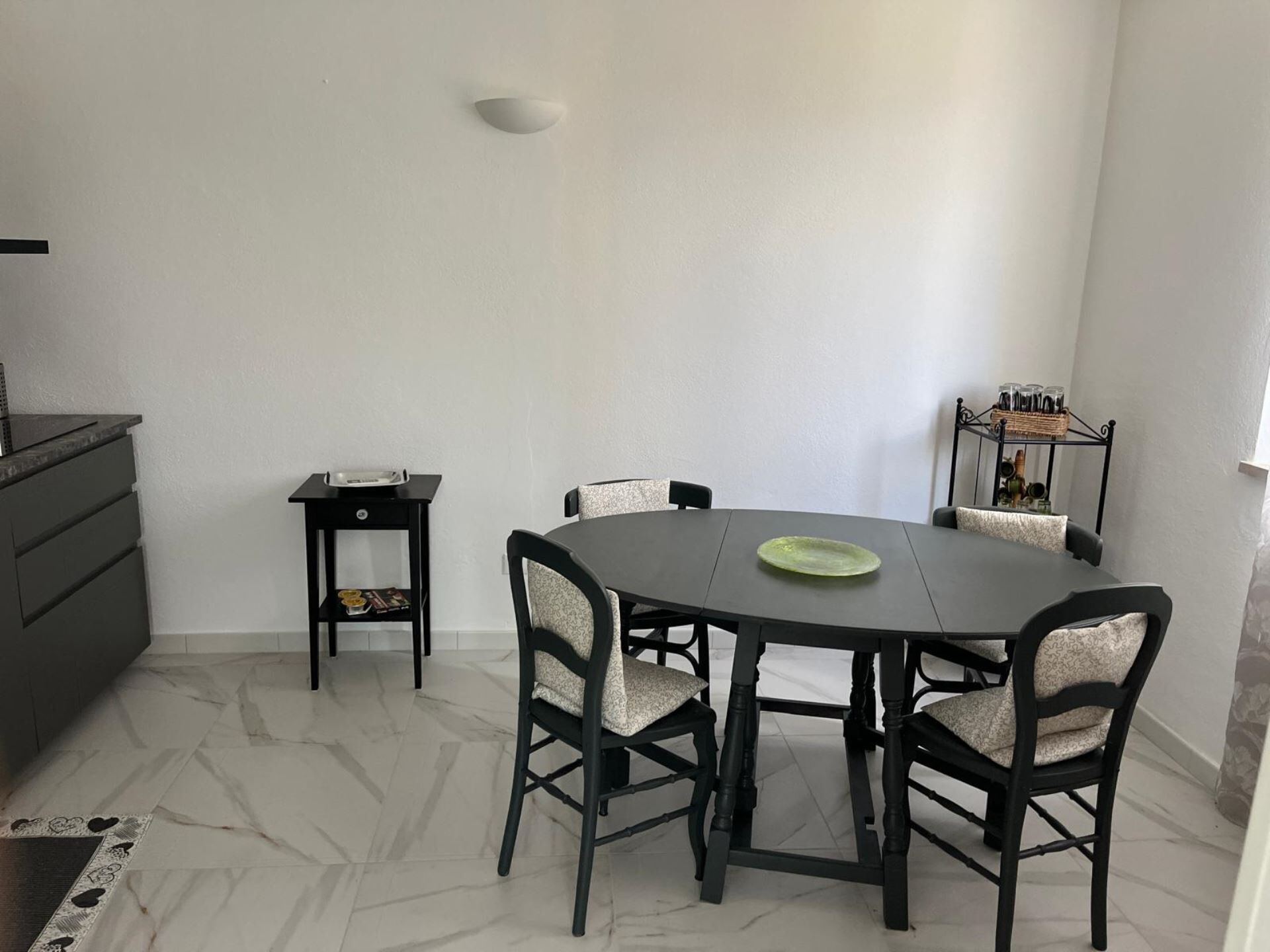 A dining area with a round table, four chairs, a small side table, and a decorative shelf with jars.
