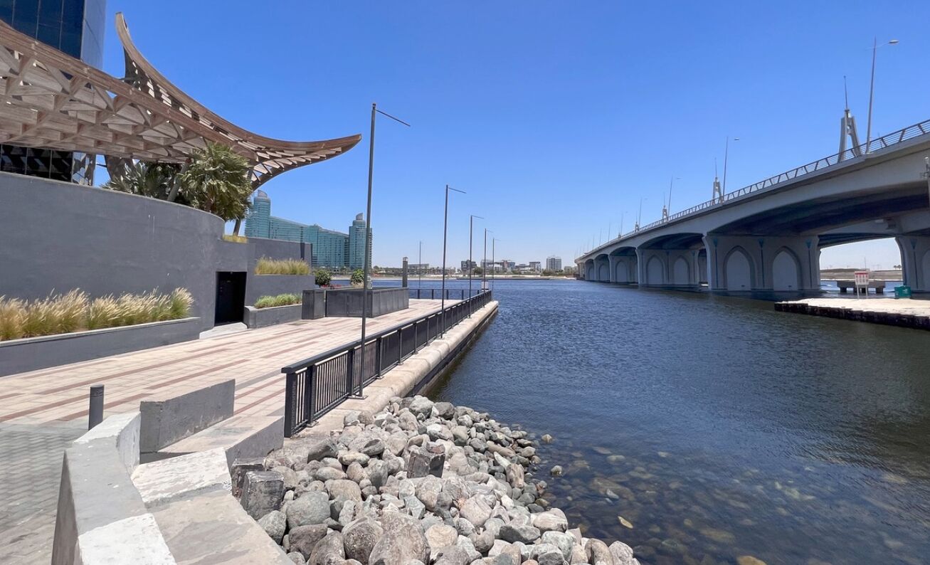 Une promenade au bord de la rivière, avec un bâtiment moderne, un pont et un ciel dégagé.