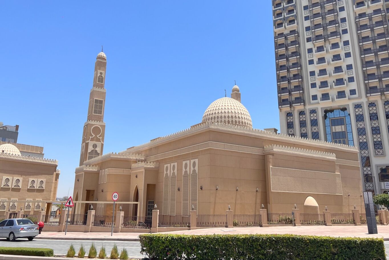 Een moskee met een hoge minaret en een grote koepel, omringd door moderne gebouwen.