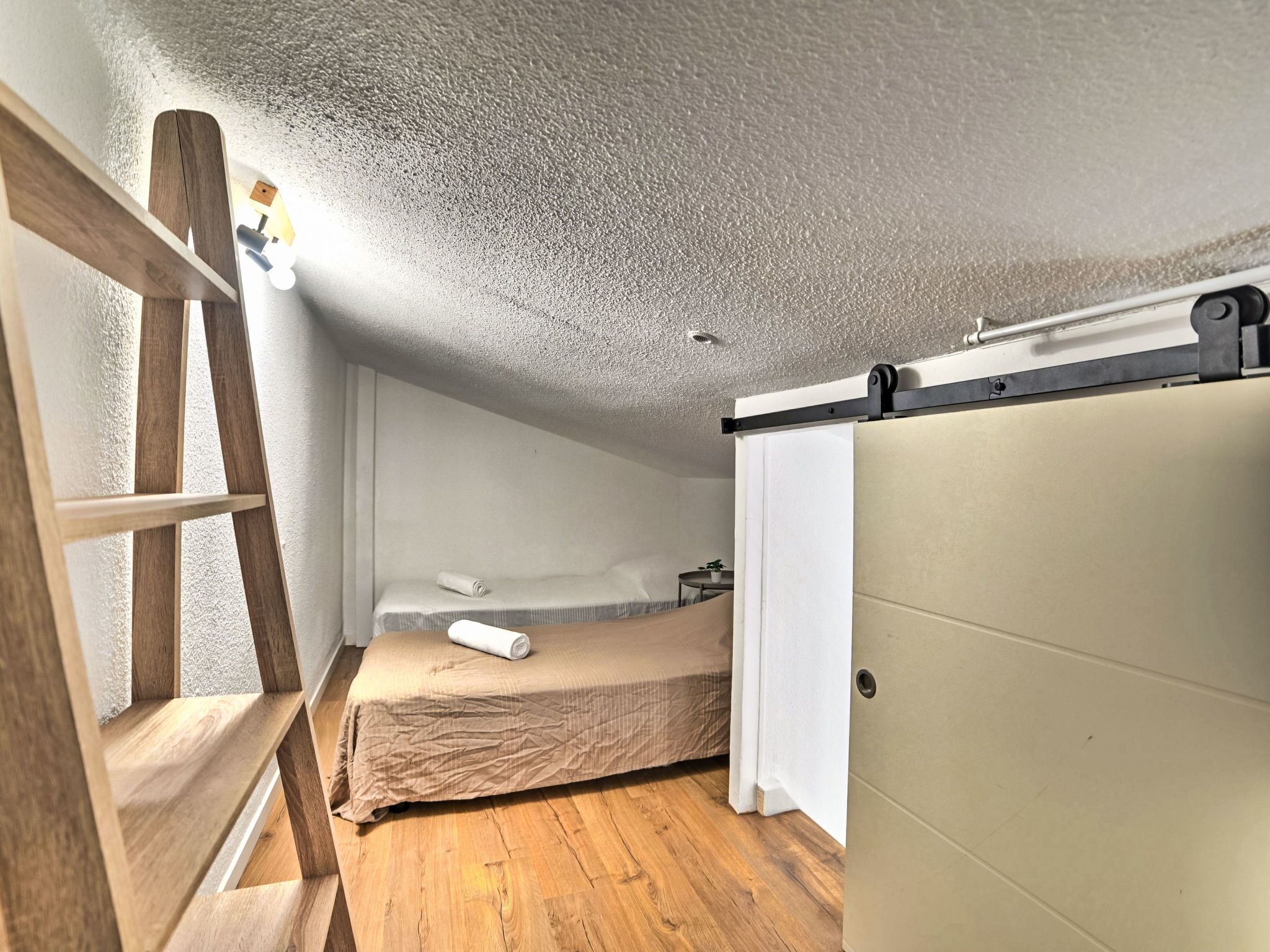 Una habitación pequeña y acogedora con una escalera de madera, una cama con un edredón enrollado y una puerta corredera.