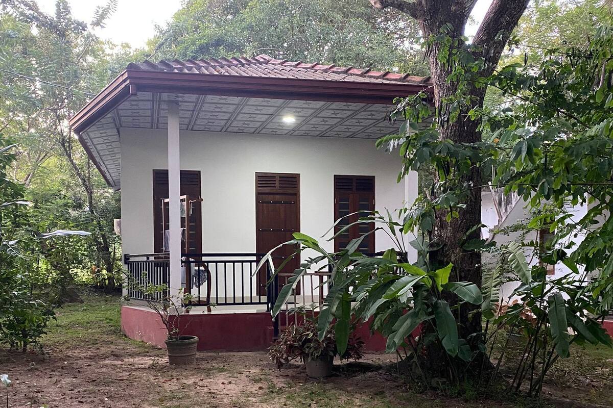 A white building with a red roof, a covered porch, and a small garden area.