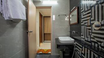 A modern bathroom with a vanity, sink, and mirror. There is a towel rack with towels, a trash can, and a patterned floor.