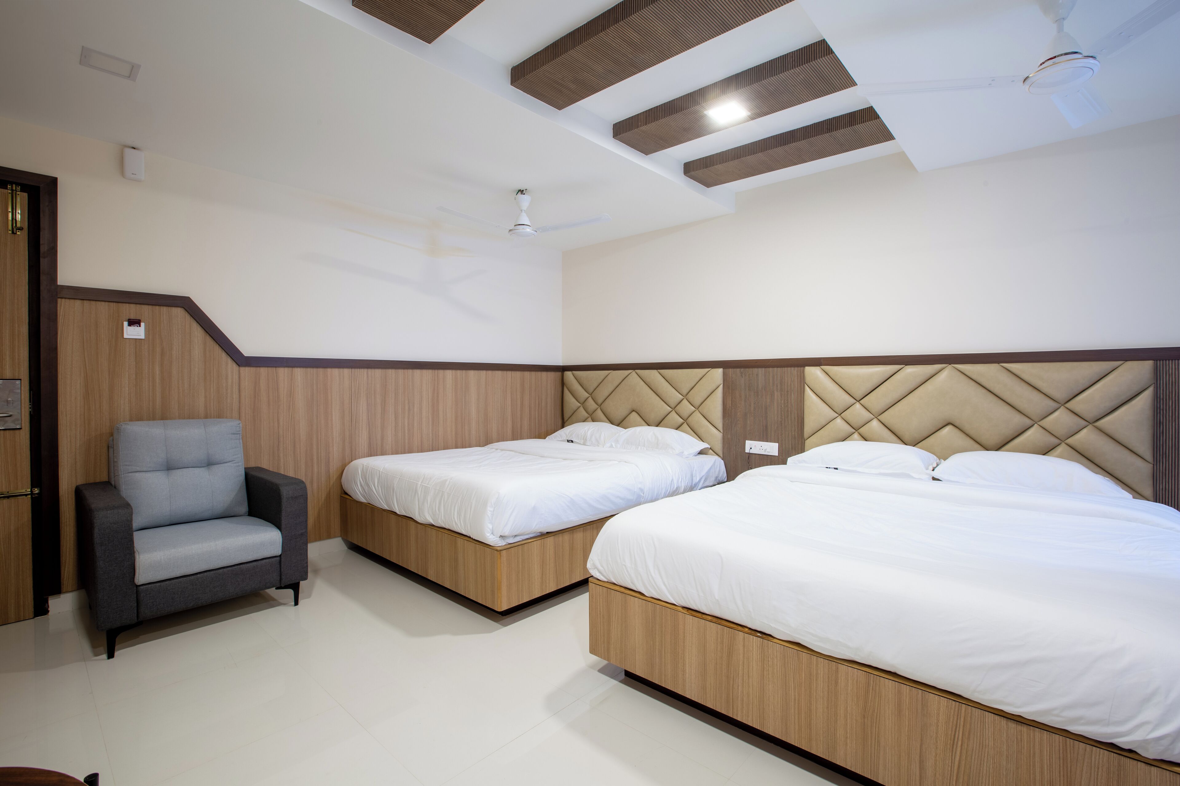 Habitación de hotel con dos camas, una silla y un ventilador de techo.