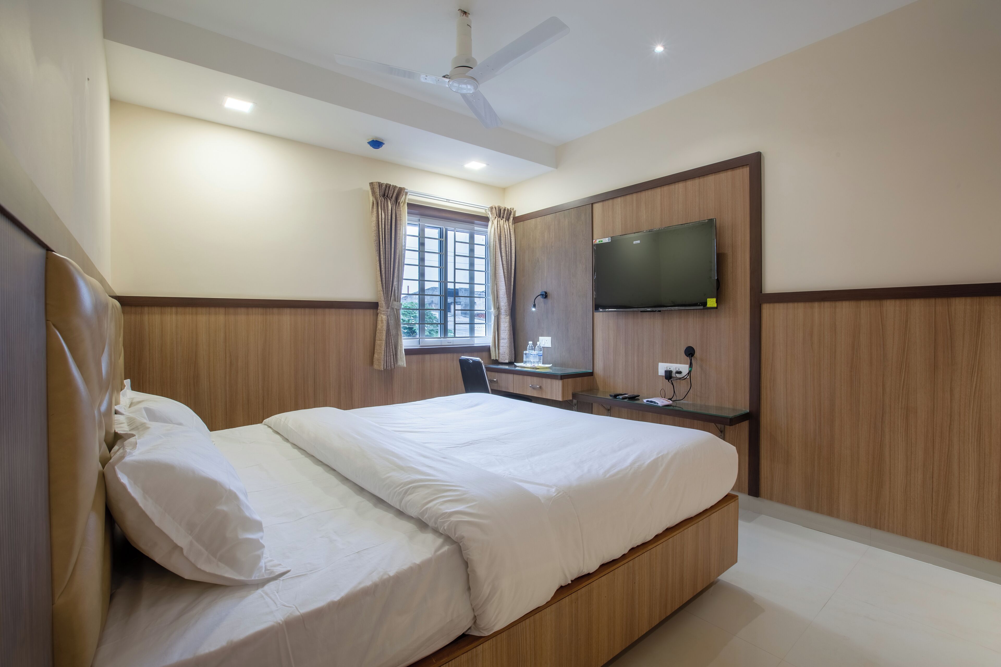 A hotel room with a bed, a desk, a chair, a TV, and a window with curtains.