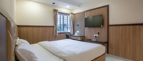 A hotel room with a bed, a desk, a chair, a TV, and a window with curtains.