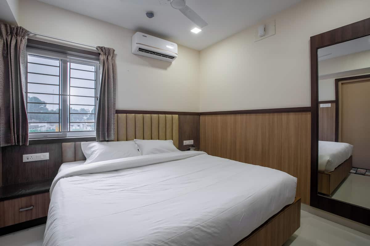 Una cama bien hecha en una habitación de hotel, con ventana, aire acondicionado y espejo.