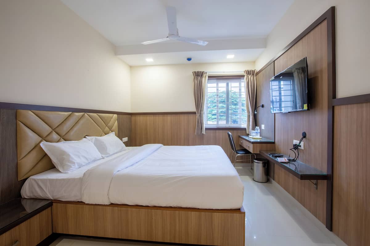 Una habitación de hotel con cama, escritorio, silla, televisor y ventana con cortinas.