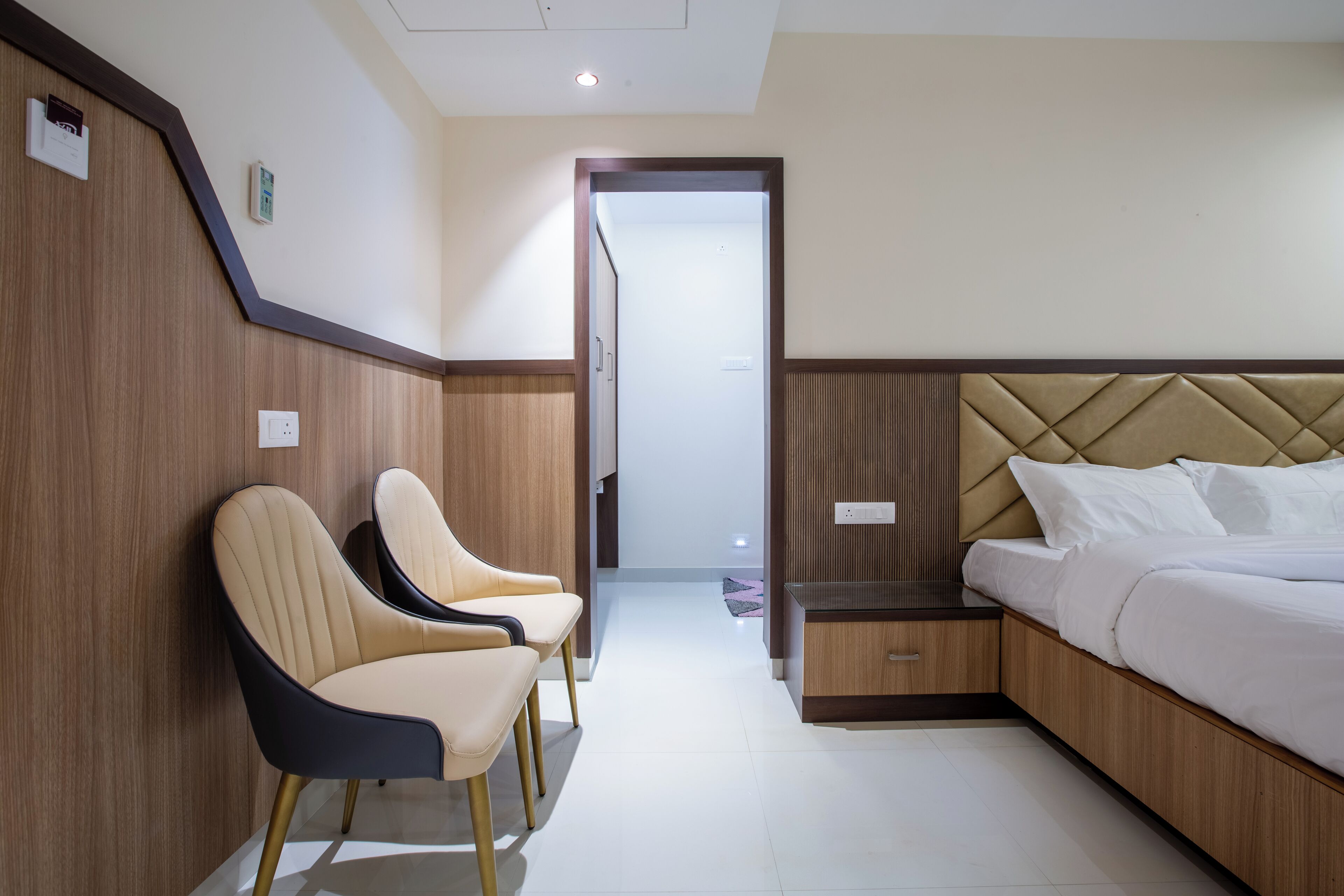 Une chambre d’hôtel avec un lit, deux chaises, une table de chevet et un mur recouvert de panneaux en bois.
