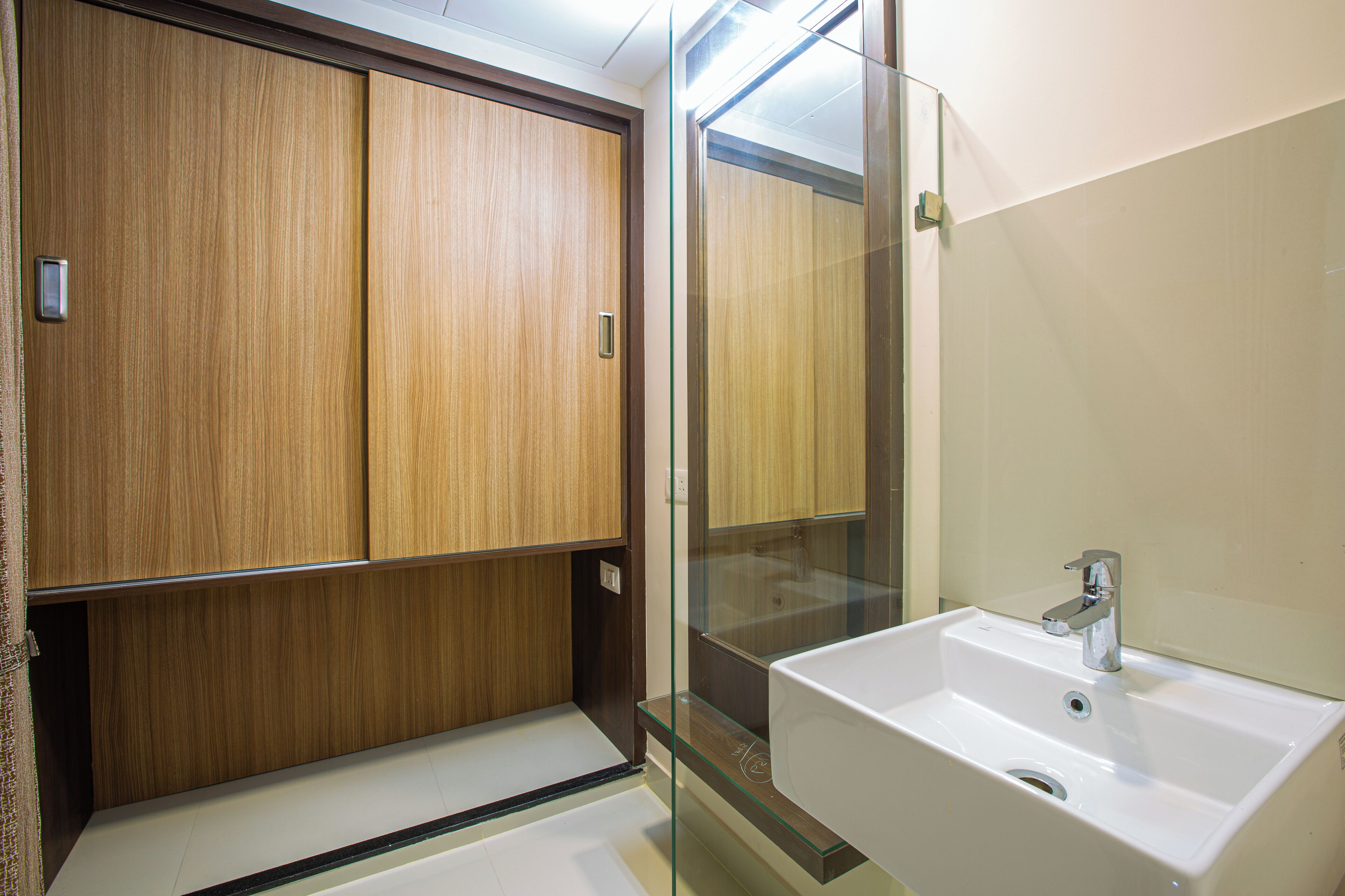 Une salle de bain avec un meuble en bois, une cabine de douche en verre et un lavabo blanc.