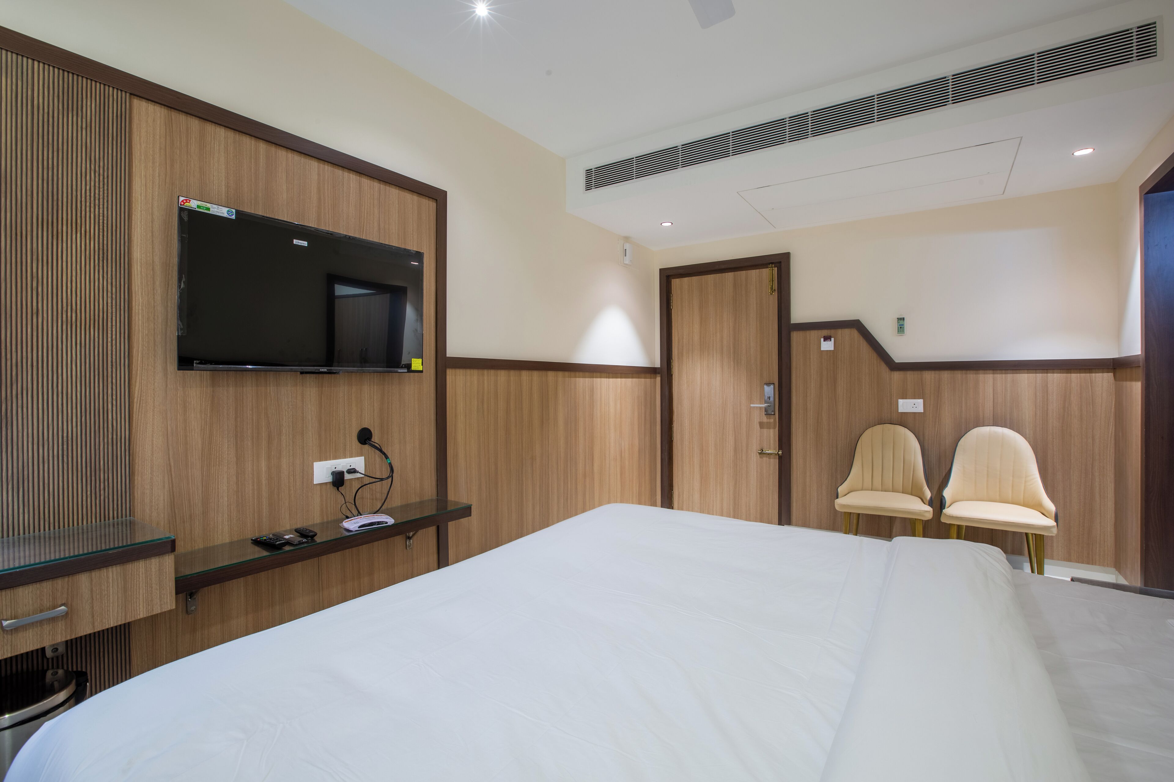 A hotel room with a large bed, a flat-screen TV mounted on the wall, a desk with a computer, and two chairs.
