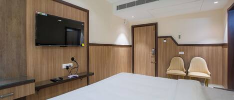 Habitación de hotel con una cama grande, un televisor de pantalla plana en la pared, un escritorio con una computadora y dos sillas.