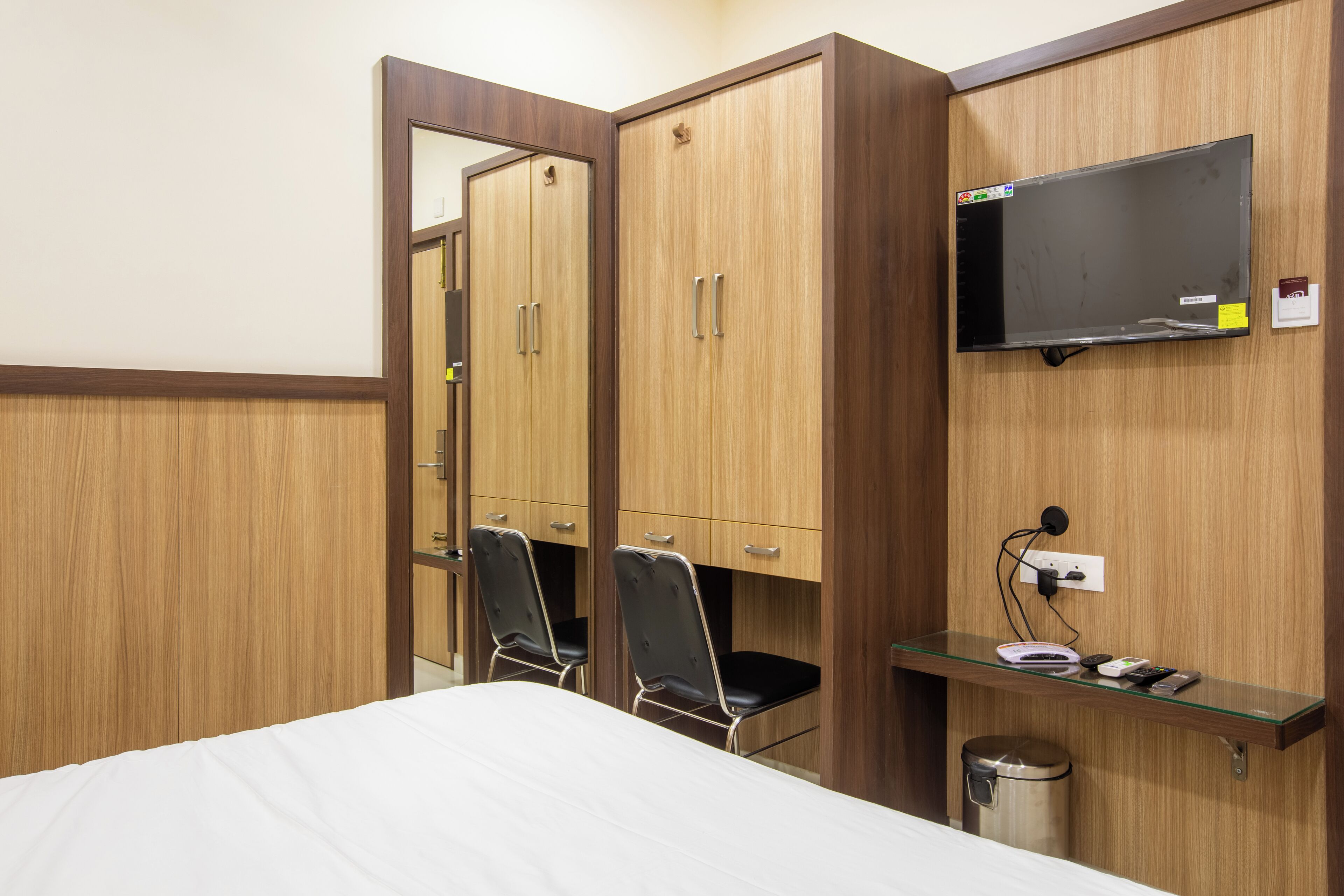 A hotel room with a bed, a desk with a flat-screen TV, a mirror, and two chairs.