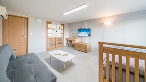 A modern living room with a grey sofa, a wooden desk, a TV, and a crib. - Namhae Yujane Pension (Namhae)