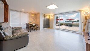 A modern living room with a leather sofa, a dining area with a table and chairs, and a large sliding glass door leading to a beach view. - Namhae Yujane Pension (Namhae)