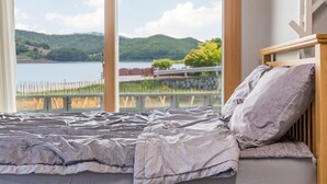 A bed with a view of a lake and hills. - Namhae Yujane Pension (Namhae)