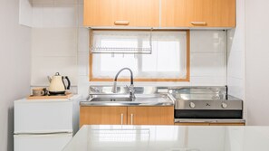 A modern kitchen with wooden cabinets, a stainless steel sink, a kettle, and a stove. - Namhae Yujane Pension (Namhae)