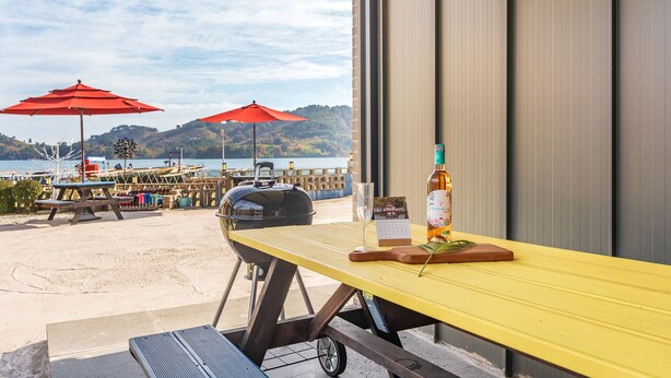 A beachside patio with a yellow table, a bottle of liquor, and a calendar. - Namhae Yujane Pension (Namhae)