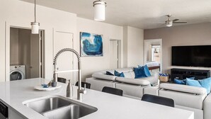 A modern kitchen with a large island, a built-in washing machine, and a flat-screen TV in the living area.