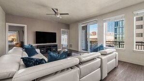 A modern living room with a large sectional sofa, a flat-screen TV, and a ceiling fan.