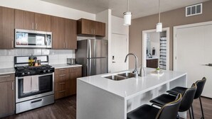 A modern kitchen with stainless steel appliances, wooden cabinets, a central island with seating, and pendant lighting.
