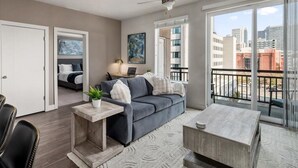 A modern apartment with a grey sofa, a small table, and a balcony with a city view.