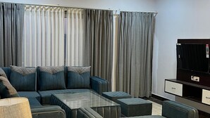 Un salon moderne avec un canapé d’angle, un pouf et un téléviseur à écran plat.
