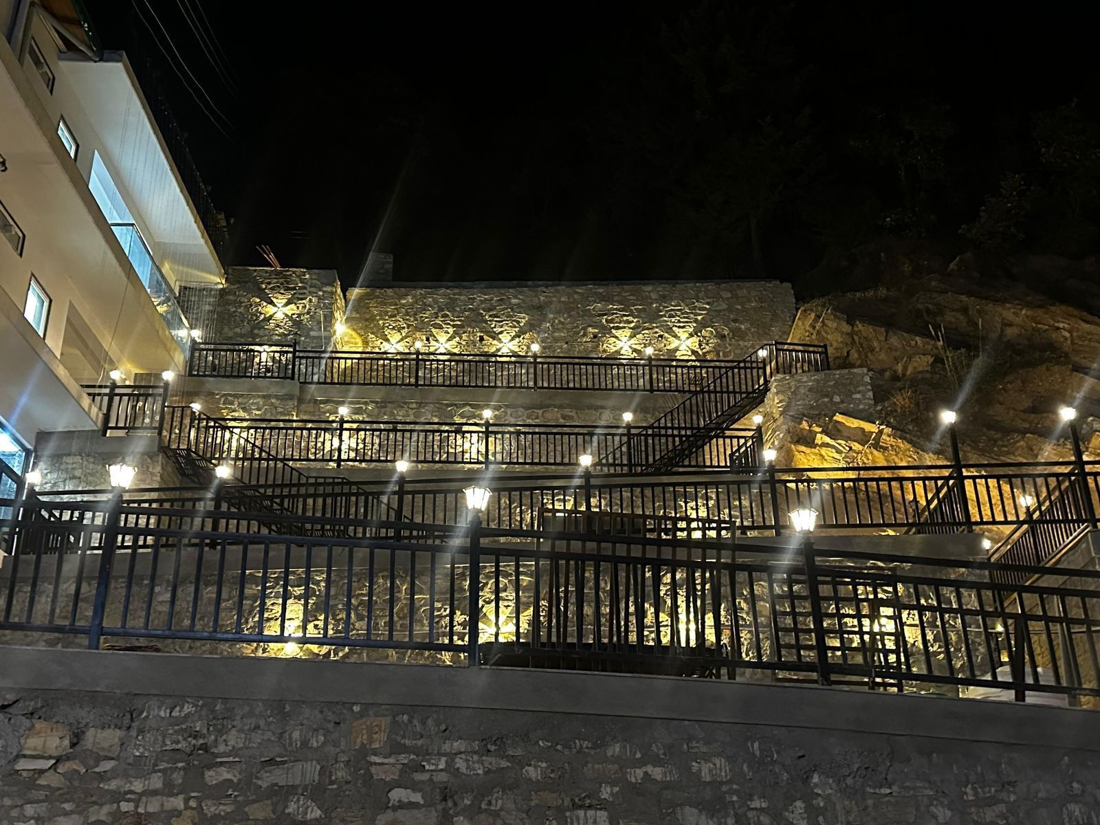 Un bâtiment en pierre à plusieurs niveaux, doté d’escaliers et de rampes d’accès extérieurs, le tout illuminé par des jeux de lumière.