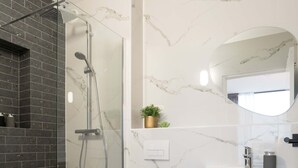 Une salle de bain moderne avec une douche à parois de verre, des toilettes blanches, un meuble-lavabo en bois et un pare-baignoire en marbre.