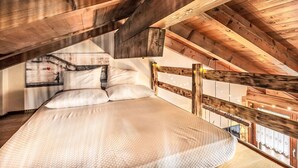 Ein Schlafzimmer unter hohen Decken mit freiliegenden Holzbalken, einem Bett mit weißer Bettwäsche und Blick nach draußen.