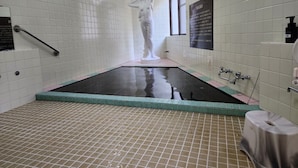 Ein Sauna-Raum mit gefliestem Boden, einem zentralen Pool und einer Statue einer Frau.