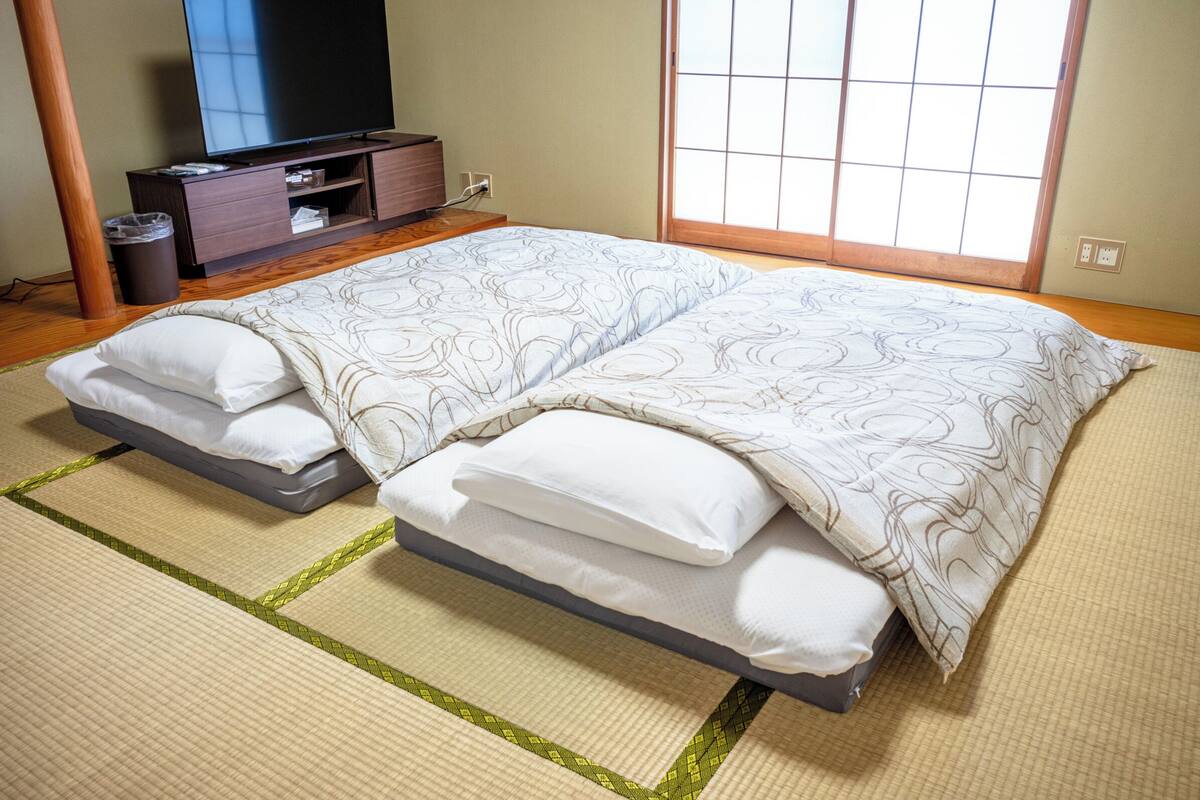 A hotel room with a bed, a TV, a wooden cabinet, and a window with a grid pattern.