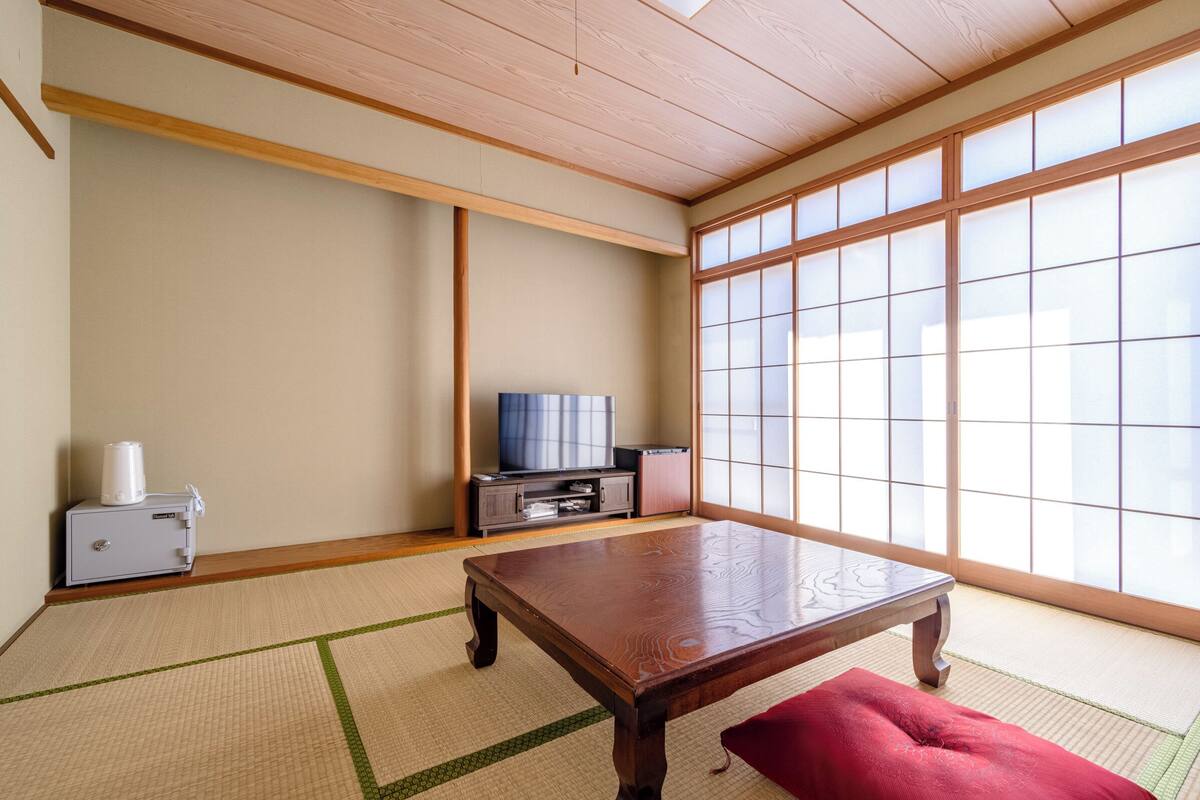 A traditional Japanese room with tatami flooring, a low wooden table, a television, and sliding shoji doors.