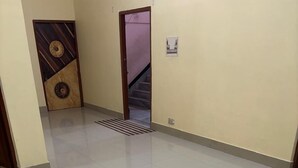 A spacious hallway with a tiled floor, a wooden door with a decorative panel, and a staircase leading to another level. - Comfort Cottage By GRB (Varanasi)
