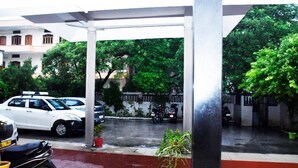 A covered parking area with a white car and a motorcycle parked. - Comfort Cottage By GRB (Varanasi)