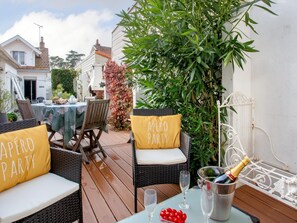 An outdoor patio with wicker furniture, a table set for a party, and a bottle of champagne. - Norecic by Interhome (La Bernerie-en Retz)