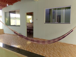Una hamaca en una habitación con piso de baldosas, techo de madera y dos ventanas.