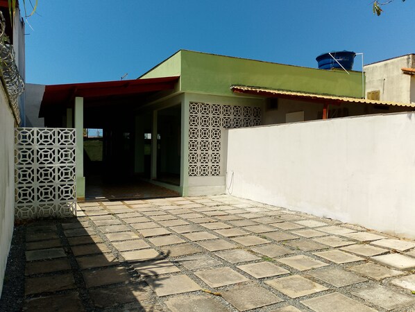 Un espacio al aire libre techado con piso de baldosas, pared blanca con diseño decorativo y un depósito de agua azul sobre un edificio.