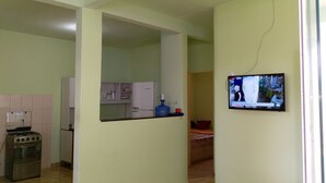 Une cuisine équipée d’une cuisinière, d’un réfrigérateur et d’un téléviseur fixé au mur.