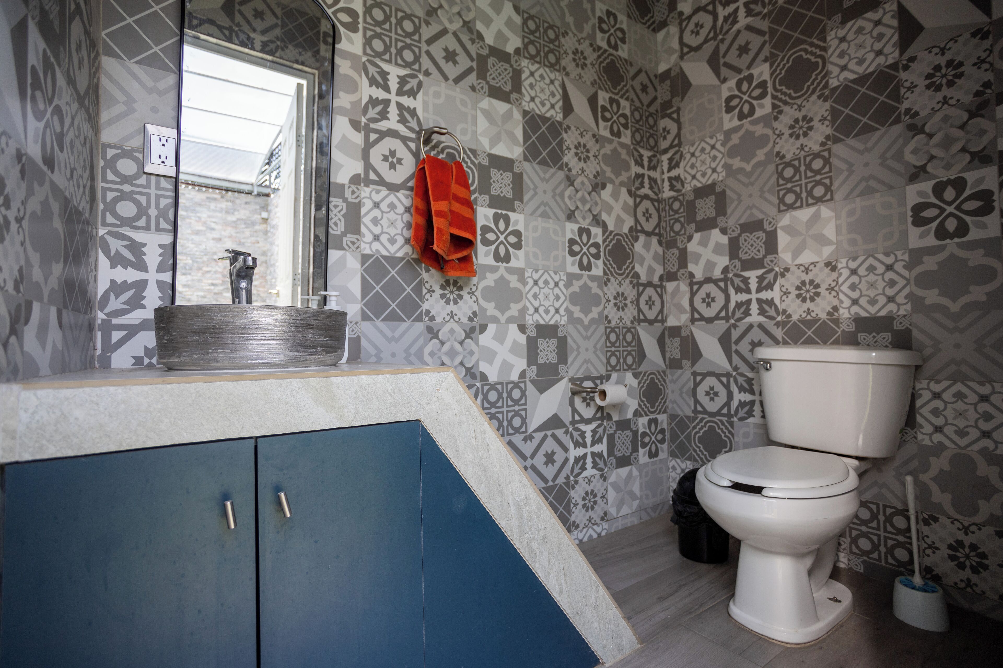 Un bagno con piastrelle decorate, un lavandino con specchio, un water e un armadietto blu.